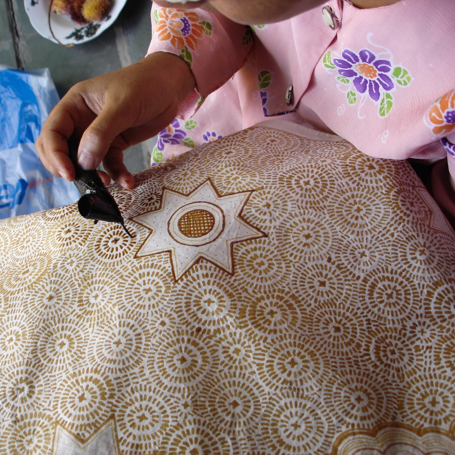 An indonesian batik artist draws on primissima cotton fabric using a batik wax pen or canting.